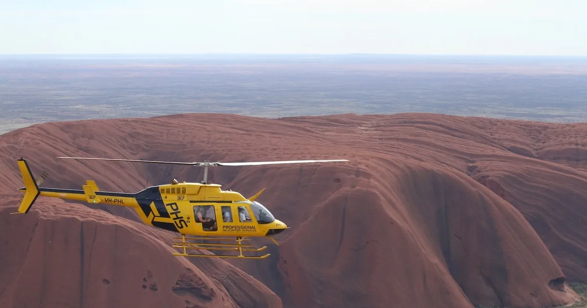 Ein gelber Hubschrauber fliegt über die rote Spitze des Uluru